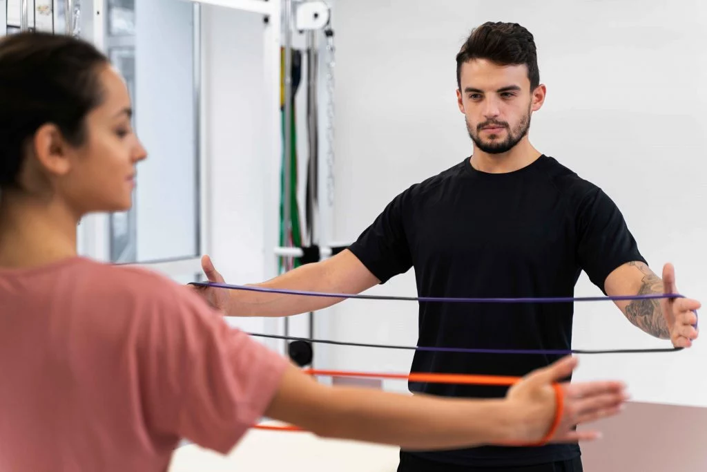 Male trainer assisting a female client with resistance band exercise.