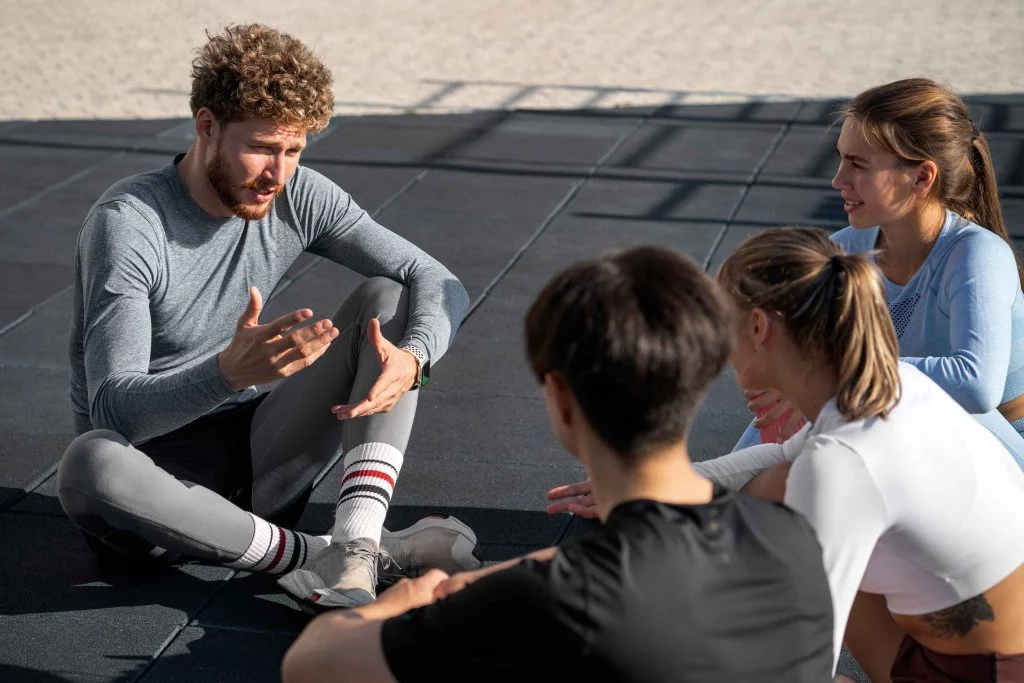 Male trainer discussing major boundaries between personal trainer and client with a group of clients during an outdoor fitness session.