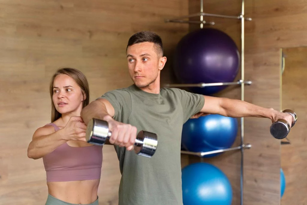 Female trainer helping a male client with proper dumbbell technique during a workout session.