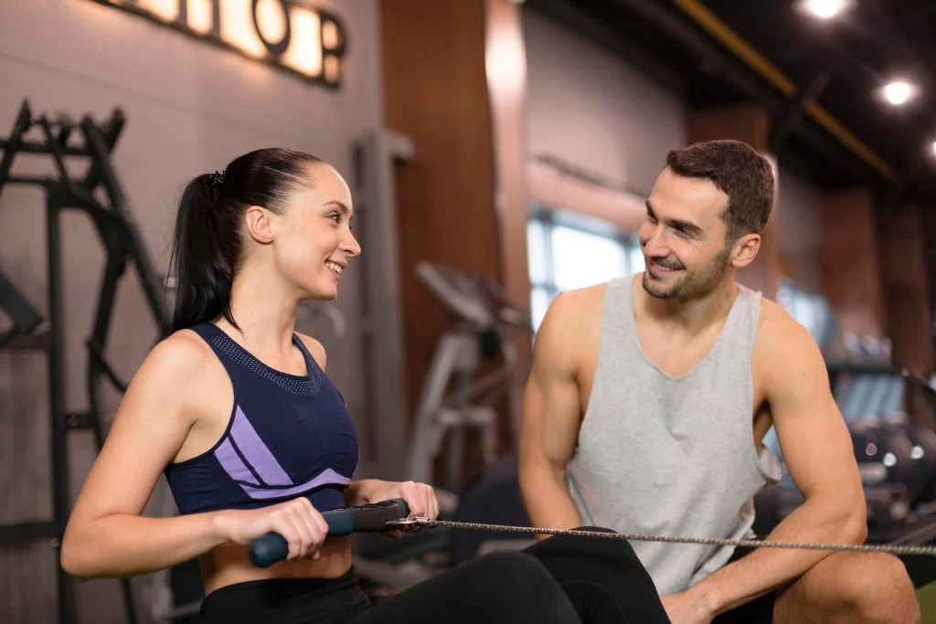 Personal trainer motivating a client during her rowing machine workout at the gym.