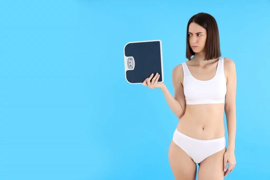 Frustrated woman checking the scale—losing inches but not weight
