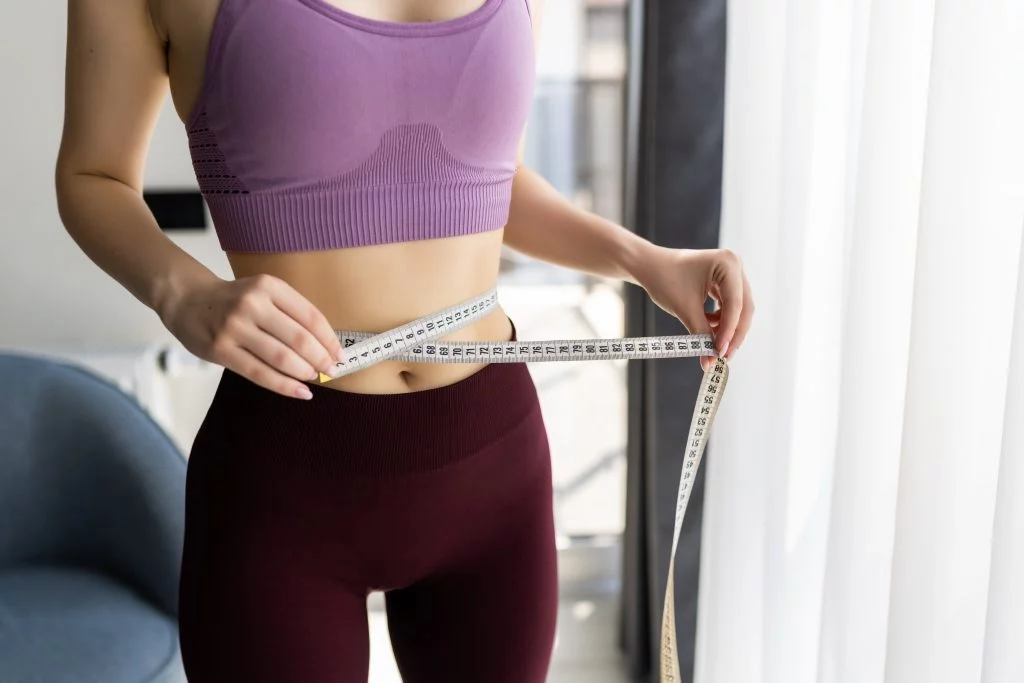 Woman measuring her waist at home to track inches lost instead of weight.
