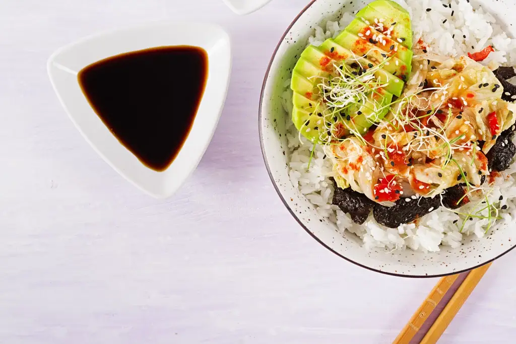 vegan-salad-with-rice-pickled-kimchi-cabbage-avocado-nori-sesame-bowl_11zon Teriyaki sauce served alongside a vibrant rice bowl with avocado, kimchi, and sesame seeds.