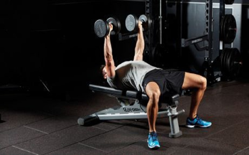 A man lying on the bench trying a bench dumbbell press as a compound chest exercise