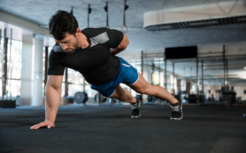 A man is doing a one-handed pushup as a chest exercise at the gym