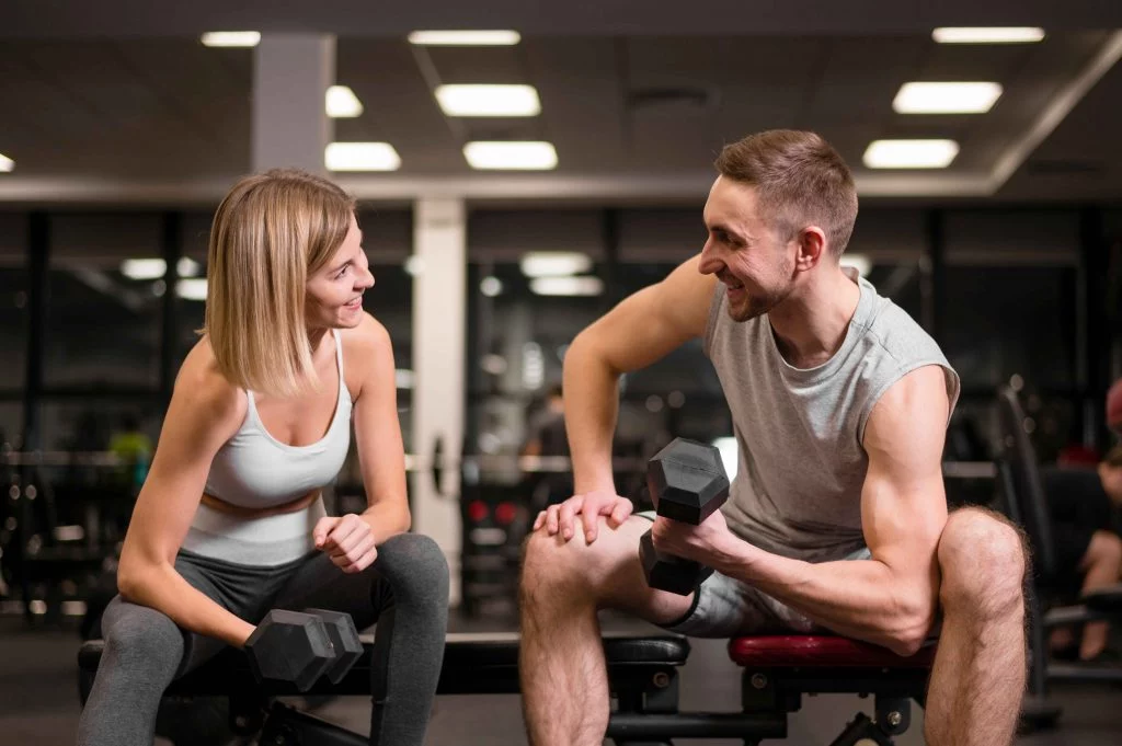 Personal trainers happy exercising together with dumbbells in a gym.