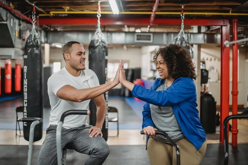Personal trainers happy high‑five on exercise bikes.