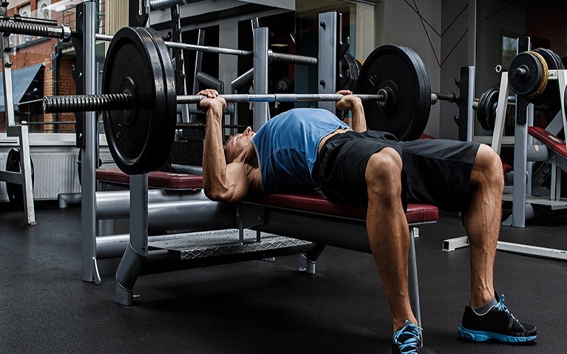 A man lying on a bench trying to do barbell bench press 