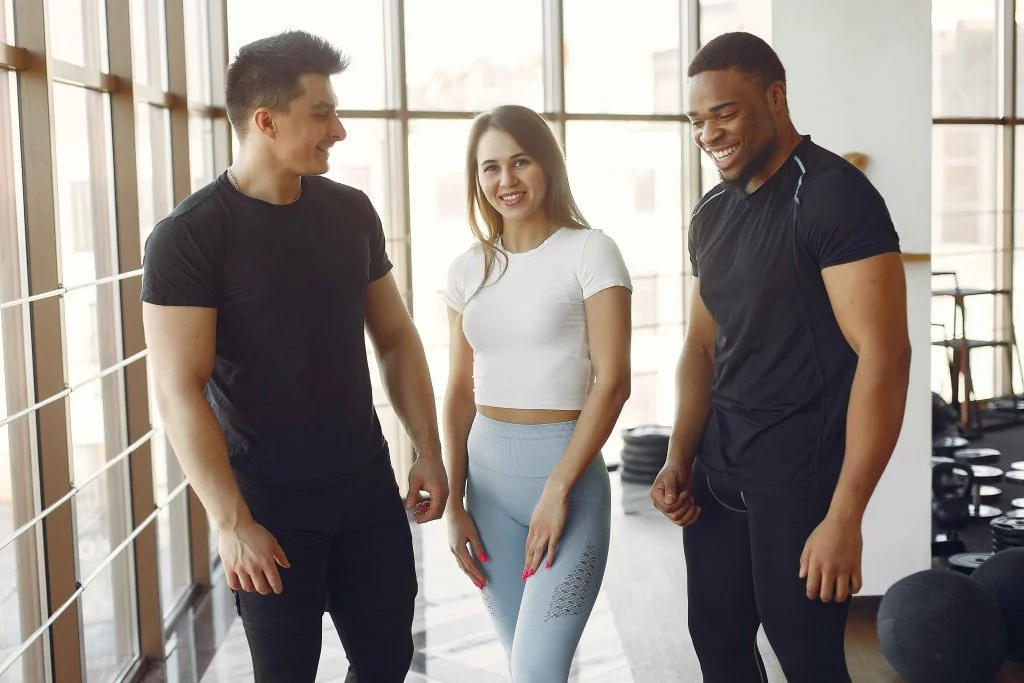 Personal trainers happy with a smiling client in a sunlit gym.