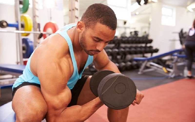 A black man is lifting a dumbbell curl as an isolation exercise