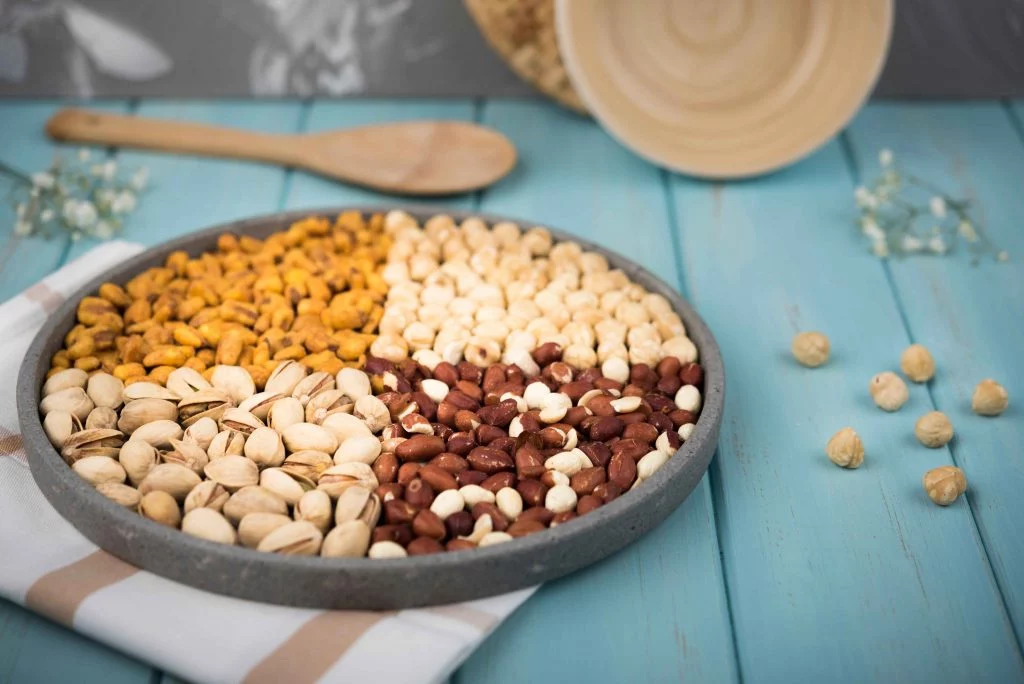 A platter of assorted nuts, including pistachios, peanuts, and roasted chickpeas, on a wooden table.