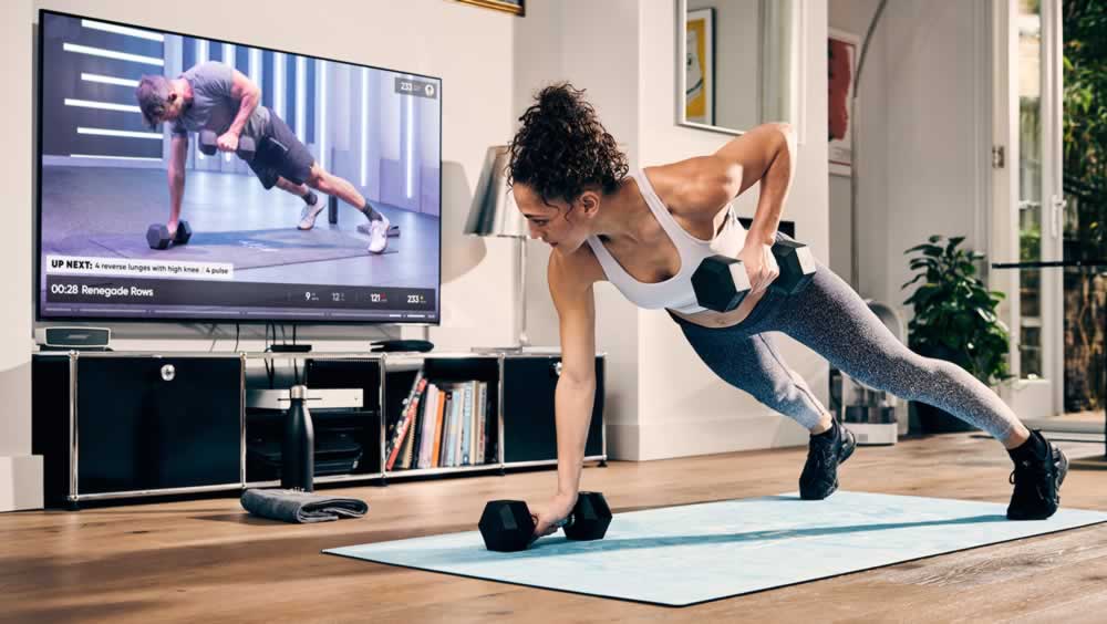 A young woman is exercising and watching her personal trainer online on a large screen