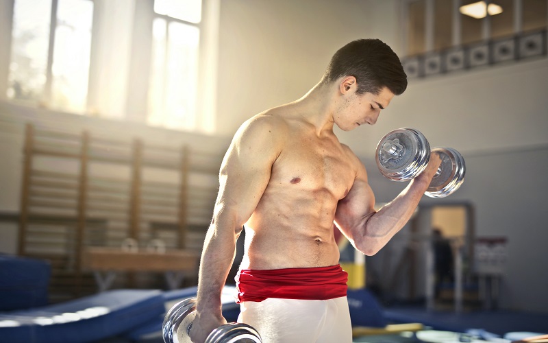 A man is working on his upper chest muscles holding two dumbbells in his hand (while he's bending his left elbow, lifting the dumbbell). 