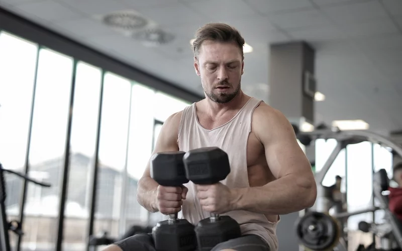 A man is exercising with heavy dumbbells at the gym