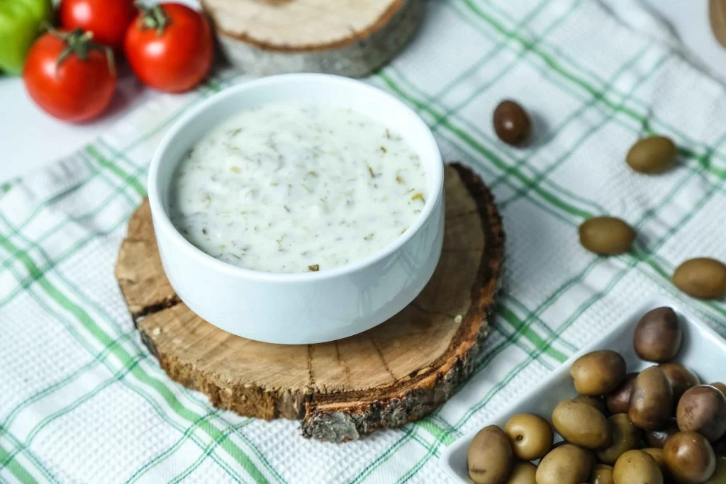 A bowl of herb-infused yogurt dip served with fresh tomatoes and olives.