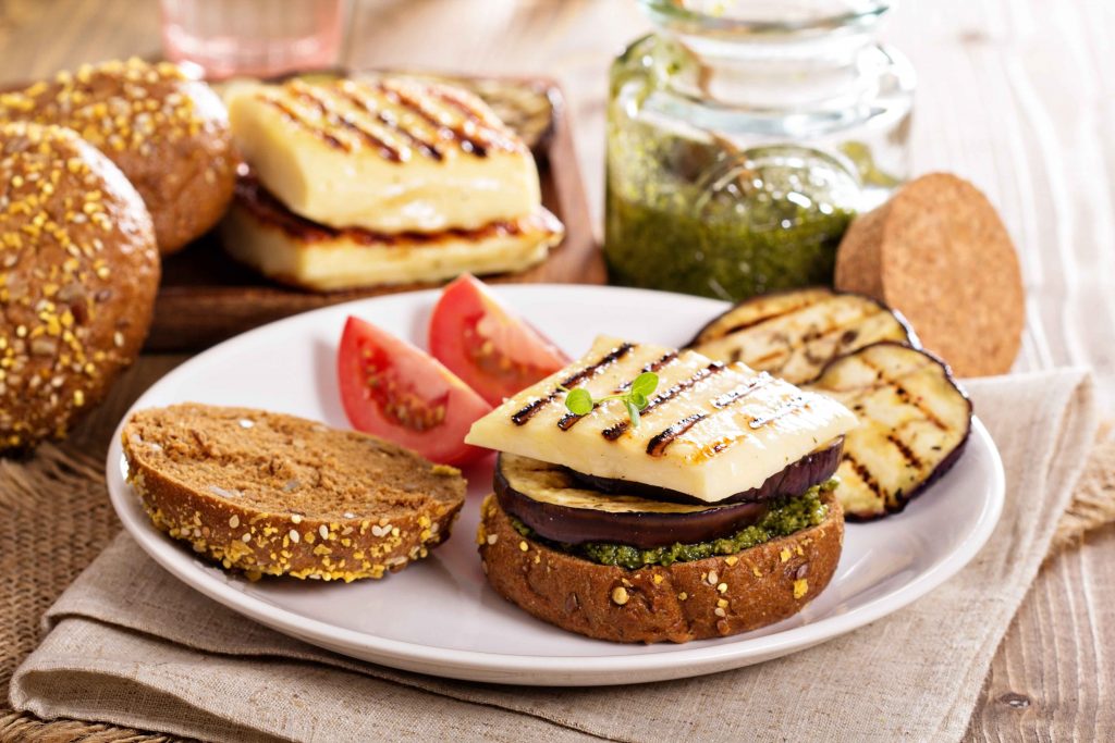 vegetarian-burger-with-cheese-eggplant-pesto_11zon A vegetarian sandwich with grilled eggplant, cheese, pesto, and sliced tomatoes on whole-grain bread.