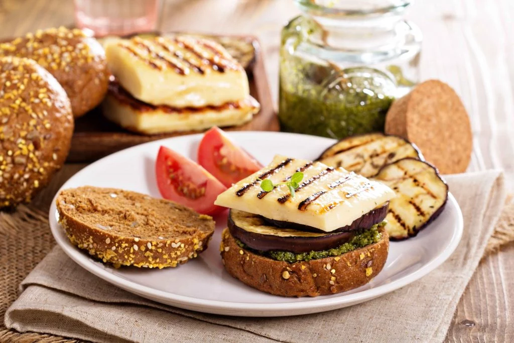 A vegetarian sandwich with grilled eggplant, cheese, pesto, and sliced tomatoes on whole-grain bread.
