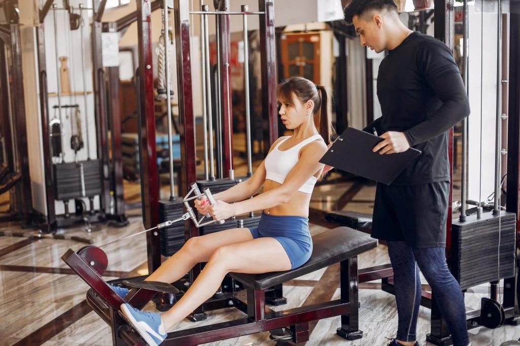 A beautiful sports couple is engaged in a gym A personal trainer supervising a woman during a strength training exercise in a gym, highlighting personalized fitness services.