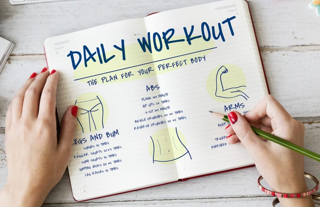 Handwriting a daily workout plan with exercises for abs, legs, and arms, designed for building the perfect body.