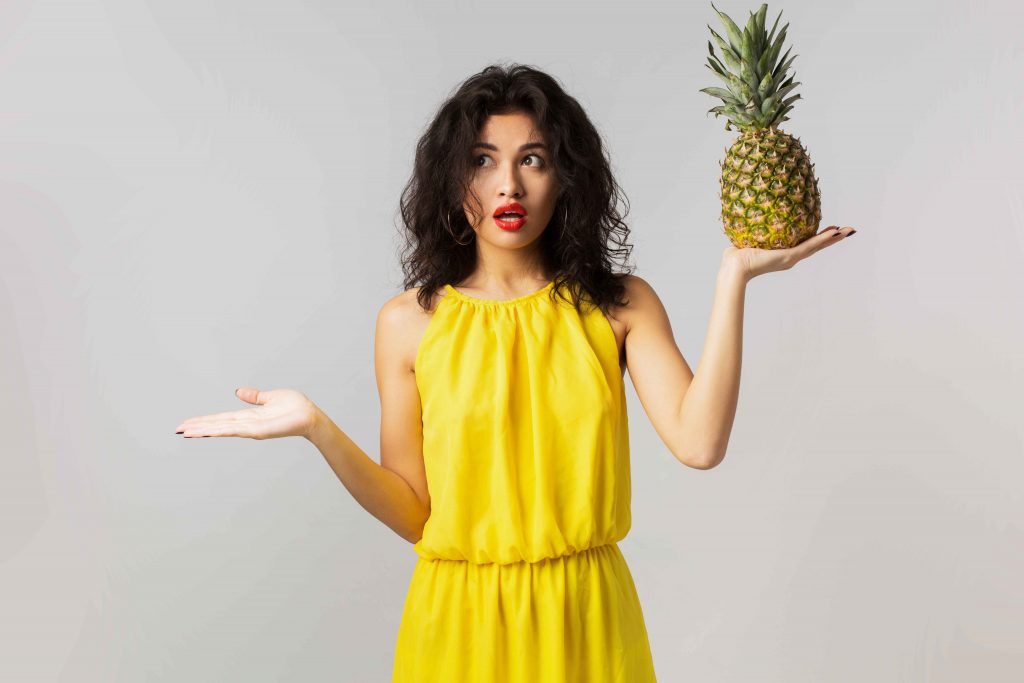 portrait-young-surprised-pretty-woman-yellow-dress-holding-pineapple-funny-emotion-shocked-face-expression-summer-style-fruit-diet-mixed-race-isolated-holding-hands-up_11zon Surprised woman holding a pineapple, exploring the benefits of Pineapple for Weight Loss.