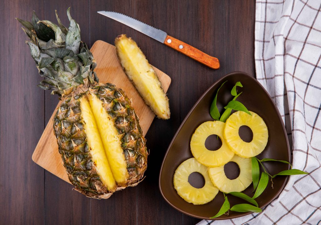 top-view-pineapple-with-one-piece-cut-out-from-whole-fruit-cutting-board-with-pineapple-slices-knife-wooden-surface_11zon Fresh pineapple slices and whole fruit, perfect for Pineapple for Weight Loss plans.