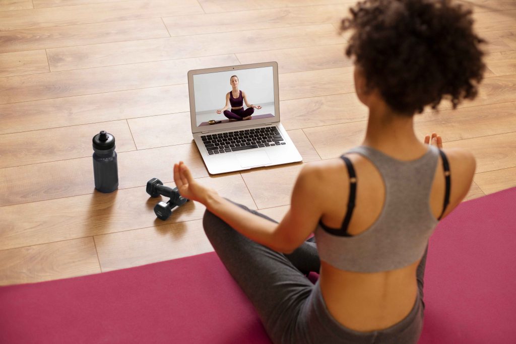 Woman doing an online training session at home with a virtual trainer on her laptop screen.
