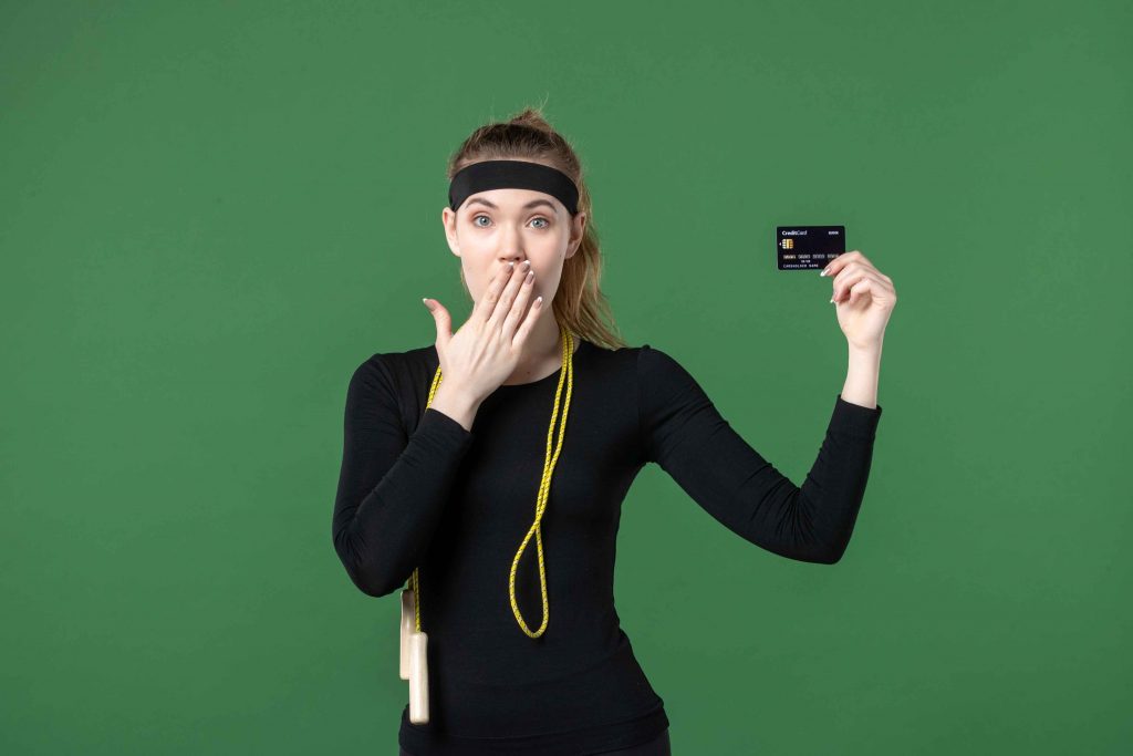 Surprised young woman in workout clothes holding a credit card—fitness cost concept.