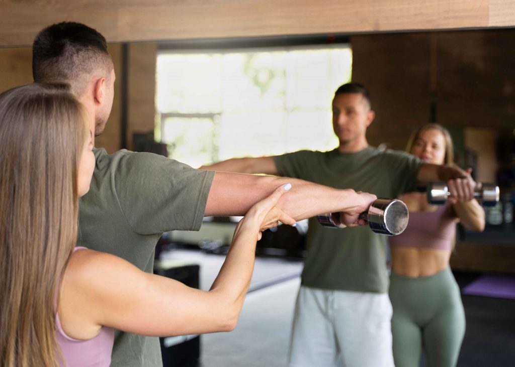 Personal trainer guiding a client during a dumbbell workout in front of a mirror.
