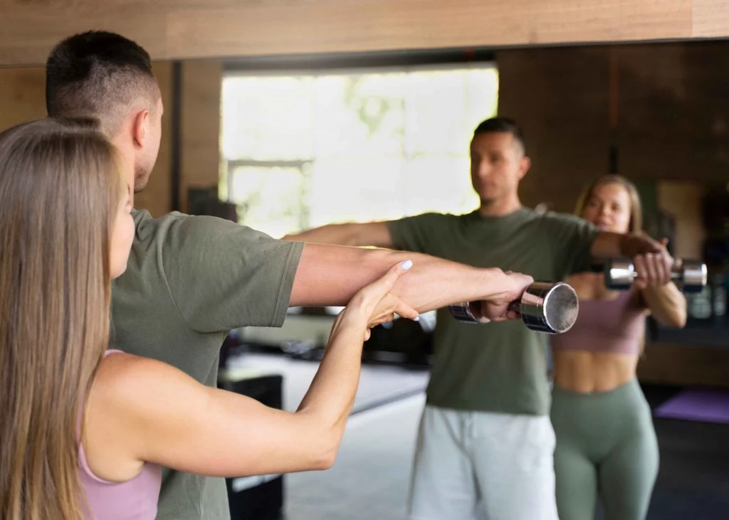 Personal trainer guiding a client during a dumbbell workout in front of a mirror.