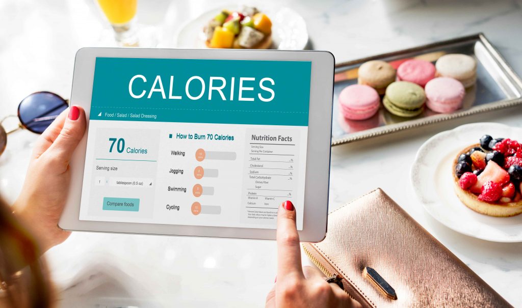 Tablet showing calorie and nutrition facts with a food comparison tool, surrounded by macarons and a fruit tart.