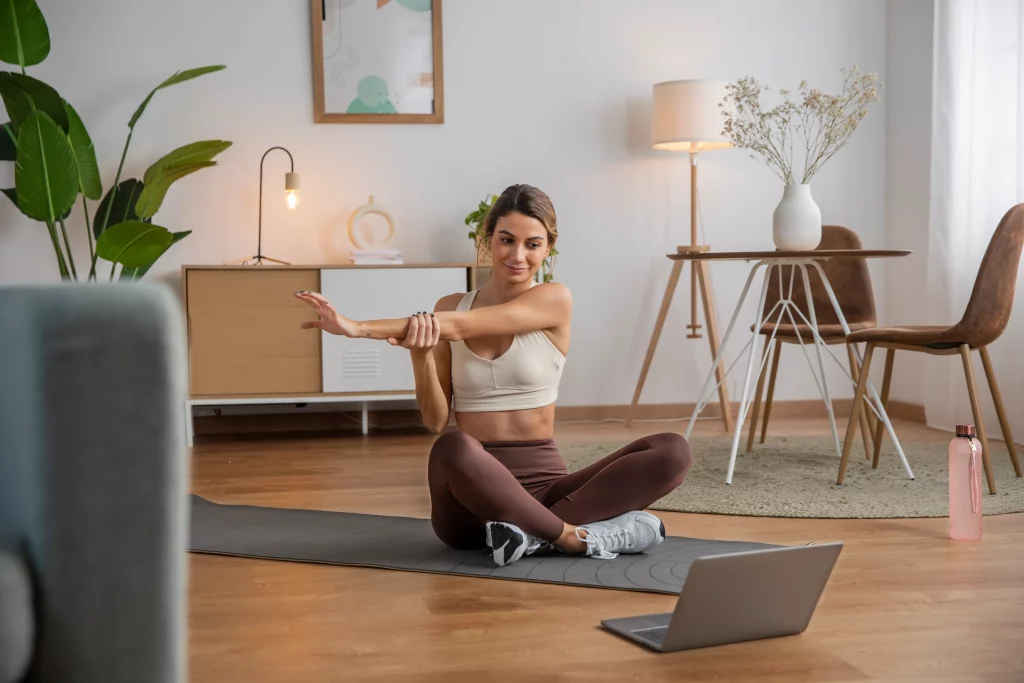 female-fitness-instructor-using-laptop-teach-class-from-home A woman doing stretching exercises during a live session with her online personal trainer.