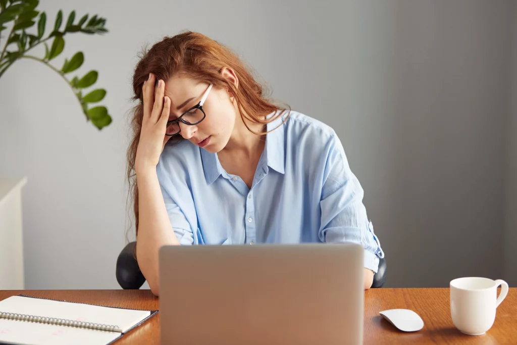 A stressed woman sitting at her desk, looking overwhelmed while thinking about trying online yoga for beginners.