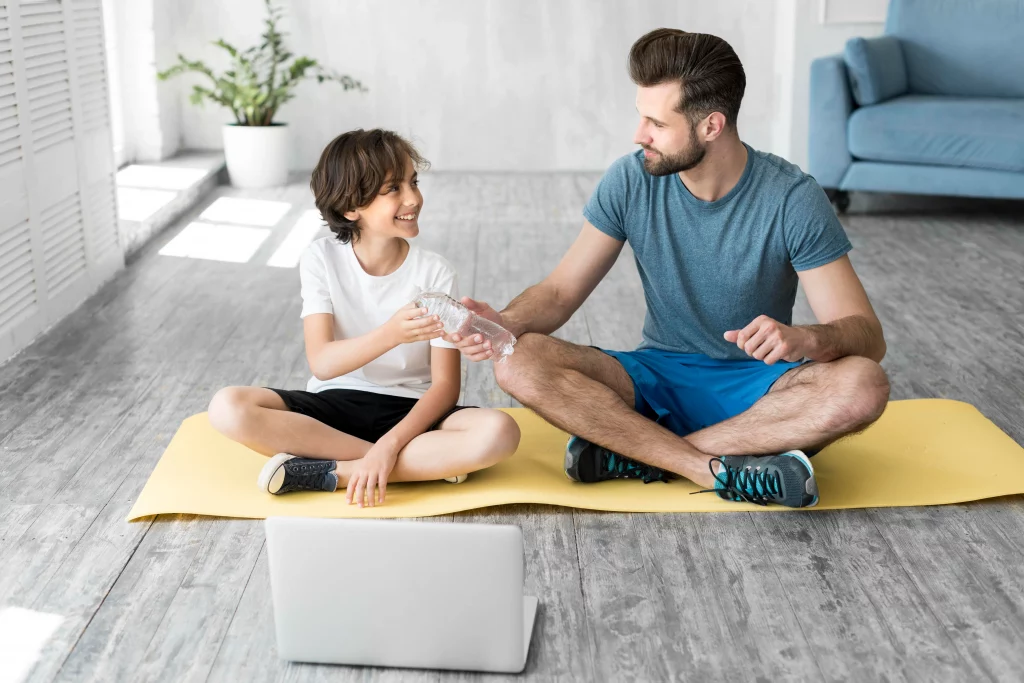 Online Personal Trainer for Your Teen A teen exercising with his dad at home while following guidance from Online Personal Trainers for Teenagers on a laptop.