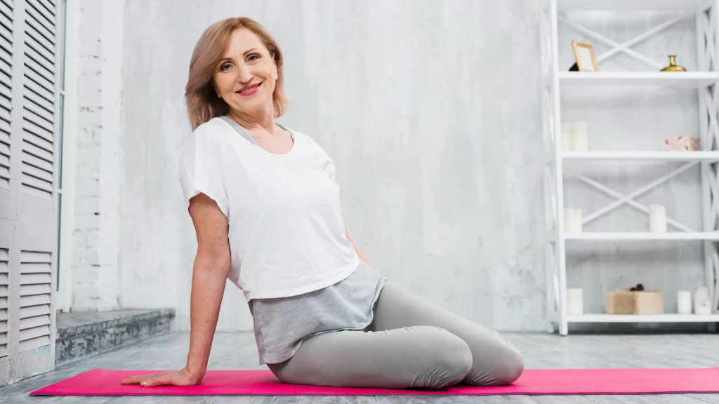 A smiling woman sitting on her yoga mat, showing a relaxed moment after a beginner yoga class.