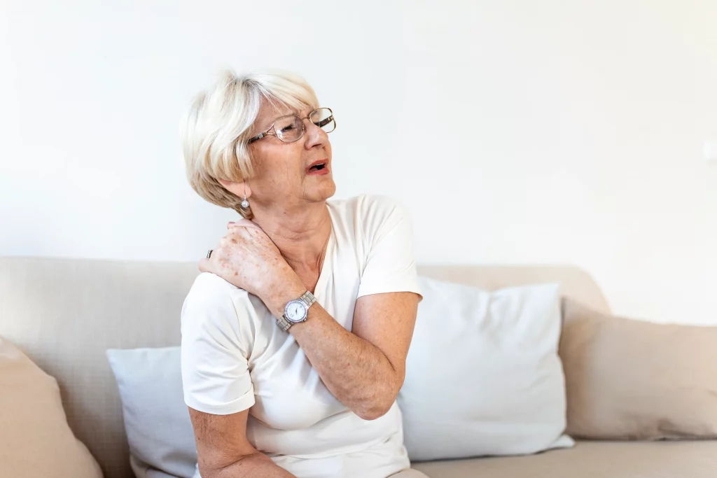 A senior woman sitting at home with neck pain, showing why guidance from an online fitness trainer for seniors matters.