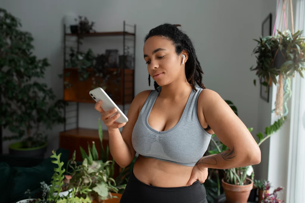 A woman is checking her phone while following guidance from a virtual weight loss coach at home.
