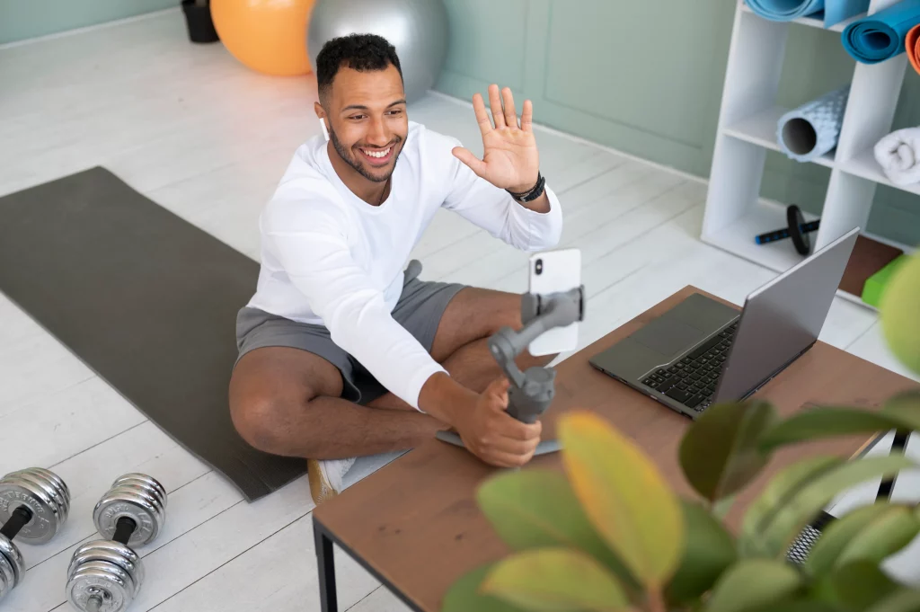 A man working out at home while greeting his online fitness trainer during a live video session.