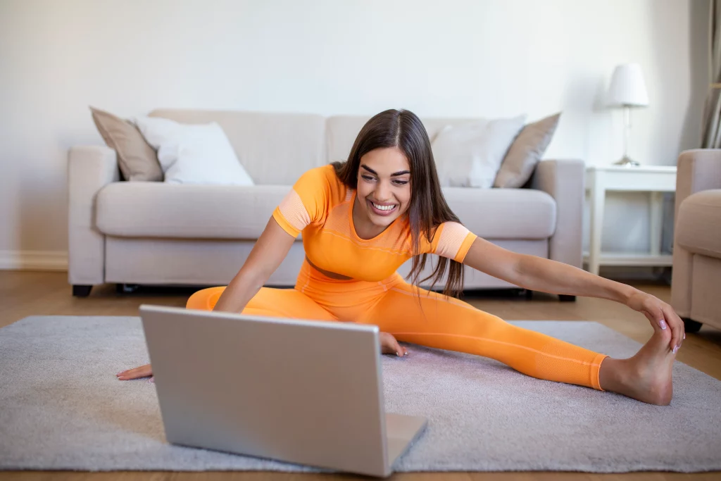 Online Yoga A woman practicing live online yoga classes at home while following a session on her laptop.