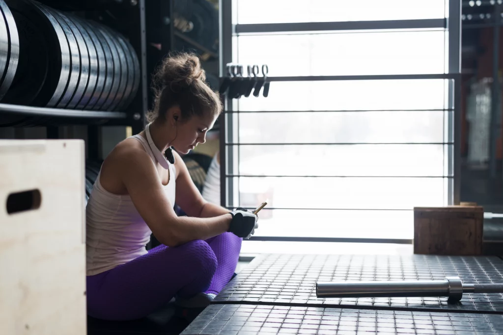 A woman checking her workout plan from a personal trainer for beginners while resting between sets at the gym.