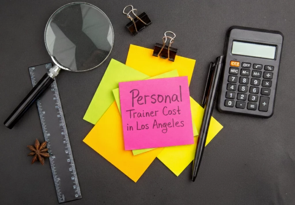 A sticky note with “personal trainer cost in Los Angeles” written on it, placed next to a calculator and a pen.