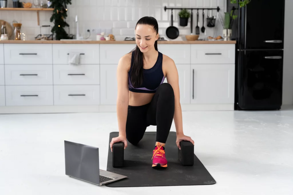 A beginner woman exercising at home while following guidance from her online fitness coach on a laptop.