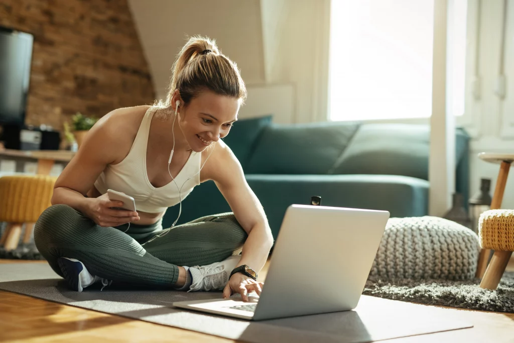 Woman joining an online personal training session from home using a laptop and earbuds.