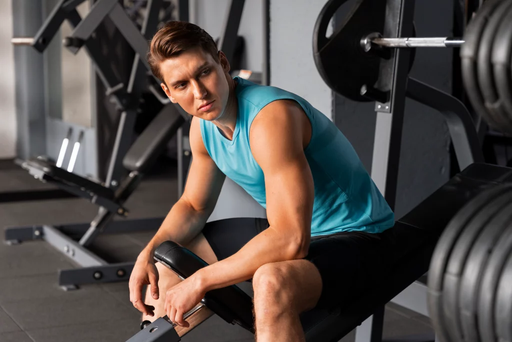 A man taking a break between sets in a gym during a training session with a personal trainer for beginners.