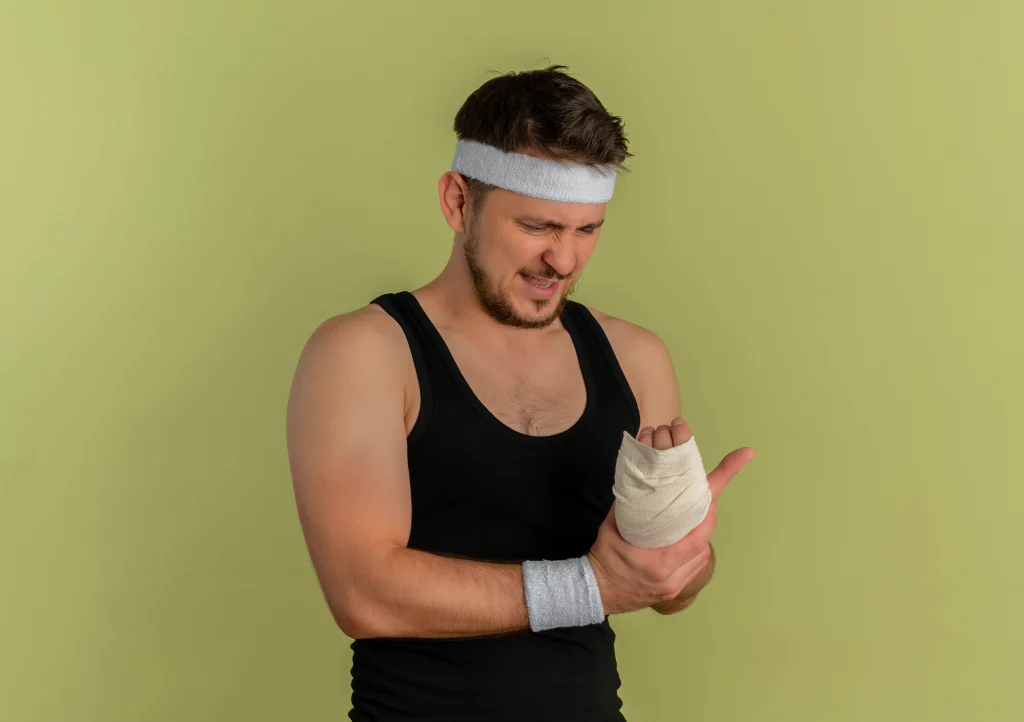 Man in sportswear holding his bandaged wrist in pain showing injury risk in training comparison between In-Person Training vs Online Training