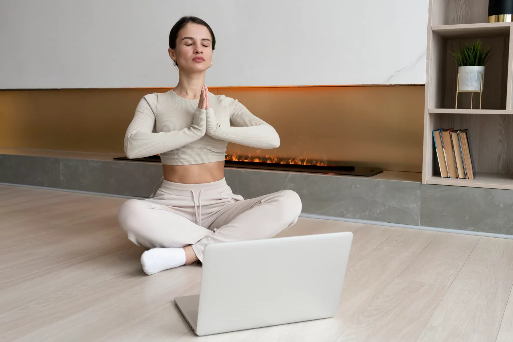 full-shot-woman-meditating-indoors Woman practicing meditation at home while following guidance from private yoga instructors through an online yoga class.
