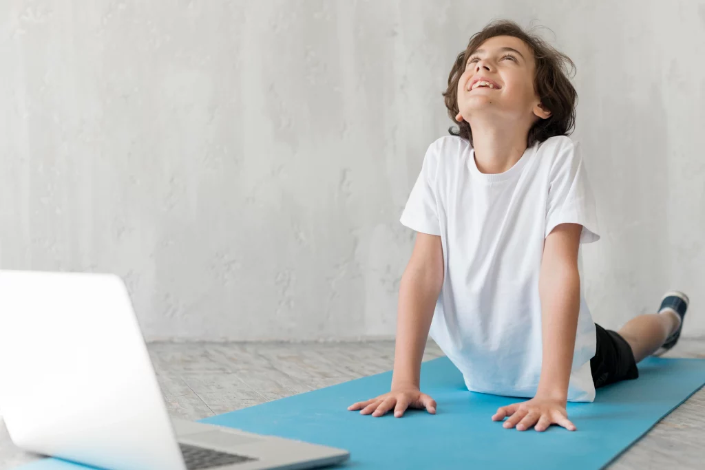 Teen participating in online yoga classes for teens at home while following a virtual instructor on a laptop. 