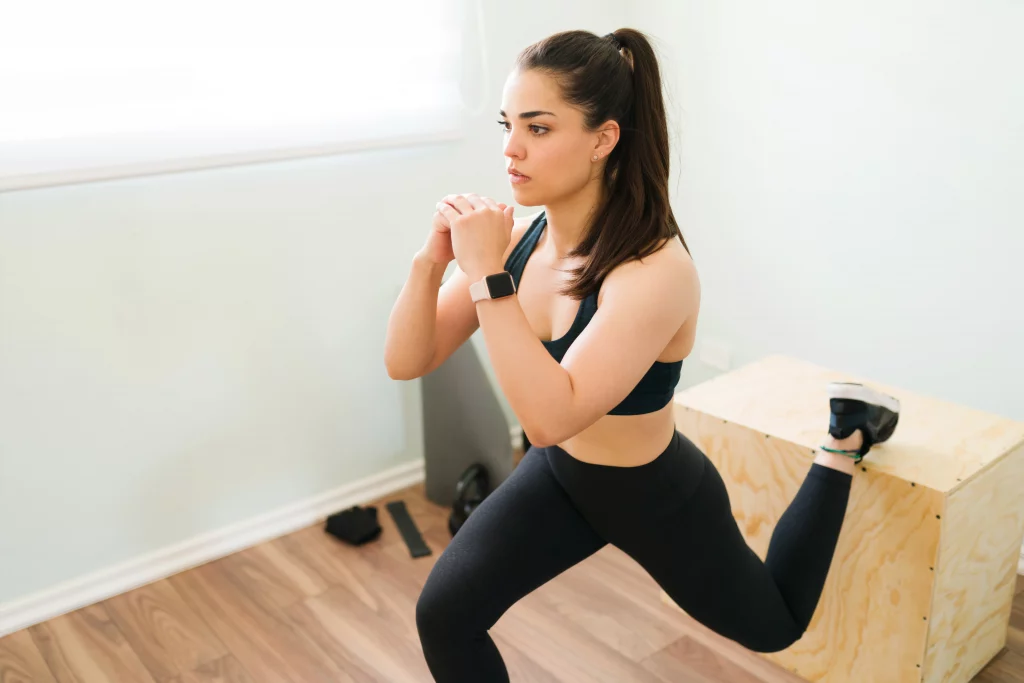 A person is performing a Bulgarian split squat with one foot elevated on a wooden box as part of best glute exercises for women