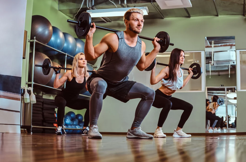 Bodybuilding personal trainer leading a group barbell squat workout in a fitness club.