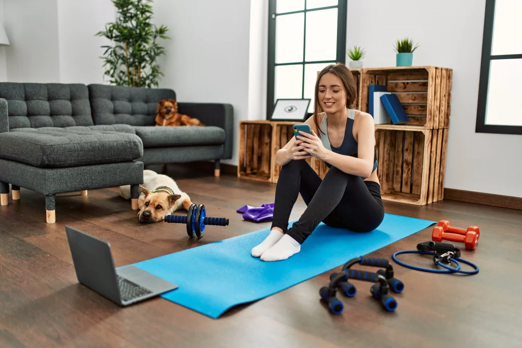 young-hispanic-woman-sportswoman-smiling-confident-using-smartphone-home A woman choosing between the best workout apps for women while preparing to exercise at home